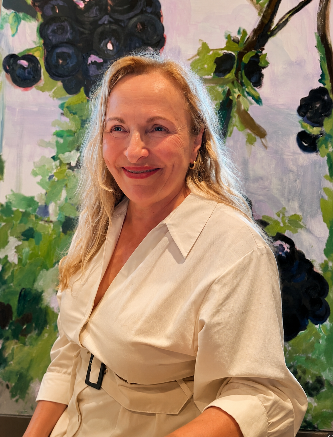 Andrea, sitzend, in heller Bluse vor einem ihrer Gemälde
